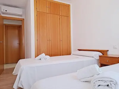 a room with two beds with white sheets and a wooden cabinet at Apartamentos Turísticos Taymar in Chiclana de la Frontera