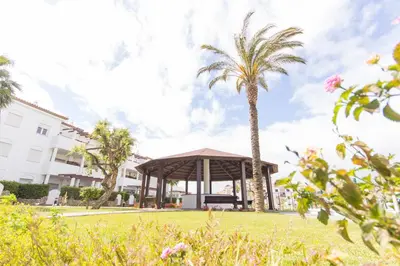 a gazebo with a palm tree and a building at Apartamentos Turísticos Taymar in Chiclana de la Frontera