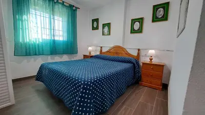 a bedroom with a bed with a blue comforter and a window at Apartamento en primera linea de playa in Novo Sancti Petri