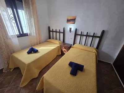 three beds in a room with yellow sheets and blue pillows at Casas el Palomar in Conil de la Frontera