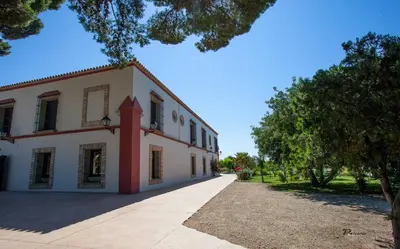 a large white building with trees in front of it at Casa Rural El Charruado in Sanlúcar de Barrameda