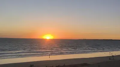 a sunset over the ocean with people walking on the beach at Apartamento RG Acciona Vistahermosa in El Puerto de Santa María