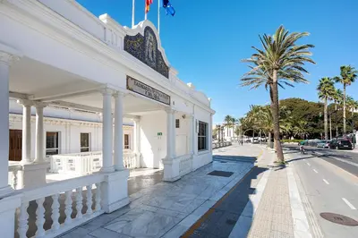a white building with a palm tree next to a street at Genteel Home Patrocinio Cádiz in Cádiz