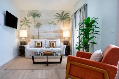 a living room with a white couch and palm trees at Genteel Home Patrocinio Cádiz in Cádiz