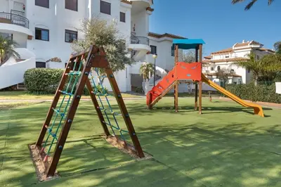 two playground equipment in a yard with a building at Barrosa Beach Apartment - Chiclana de la Frontera in Novo Sancti Petri