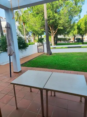 a white bench sitting under an umbrella on a patio at Apartamento planta baja con jardín privado in Novo Sancti Petri