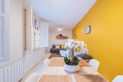 a dining room with a table and a yellow wall at Cadizz Anda La Luz Tu lugar en El Puerto Santa María centro ciudad in El Puerto de Santa María