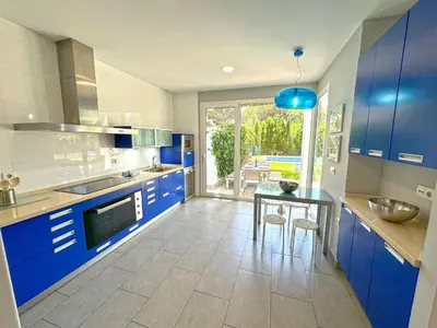 a kitchen with blue cabinets and a table with chairs at Villa el Cenador, Urb Roche Conil in Roche