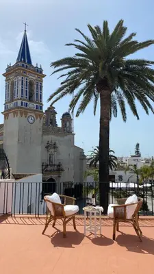 two chairs and a table in front of a building with a palm tree at Casa Michel in Chipiona
