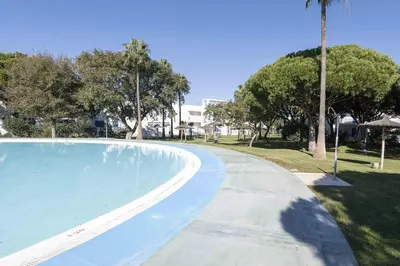 a swimming pool in a park with a palm tree at La Almadraba in Novo Sancti Petri