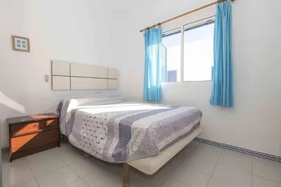 a bedroom with a bed and a window with blue curtains at La Almadraba in Novo Sancti Petri