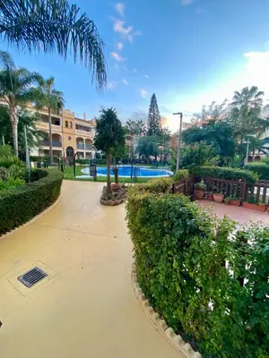 a walkway through a park with trees and a building at Playa Ballena Apartment in Chipiona