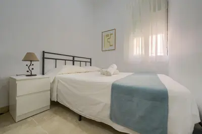 a white bedroom with a bed and a night stand at Apartamento Playa de Cádiz in Cádiz