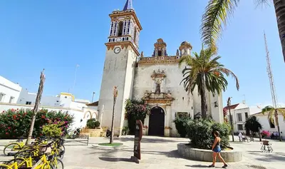 a woman walking in front of a building with a clock tower at YourHouse Apartamentos Andasol 1D in Chipiona