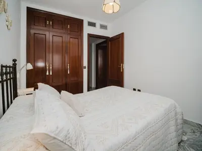 a white bed in a bedroom with a wooden door at Winahost Apartamento Sanlúcar de Barrameda in Sanlúcar de Barrameda