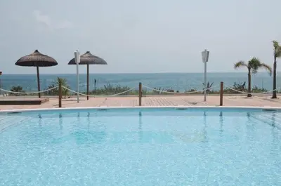 a large swimming pool with umbrellas and the ocean at Apartamento Chiclana playa in Poblado de Sancti Petri