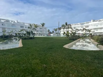 a large grassy field with buildings in the background at Nuevo bajo con gran jardín en primera línea playa in Chipiona