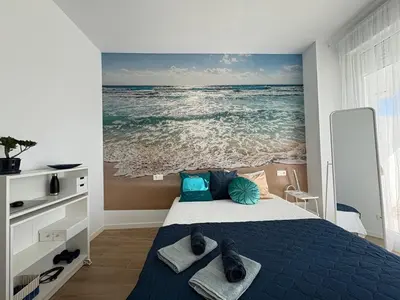 a bedroom with a bed with a painting of the ocean at Nuevo bajo con gran jardín en primera línea playa in Chipiona