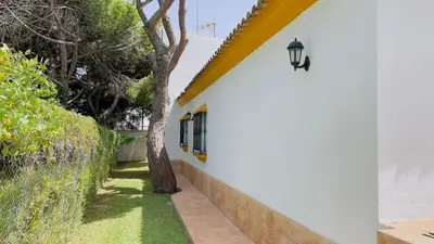 a white building with a tree next to a sidewalk at Avenida de los Pescadores in Novo Sancti Petri