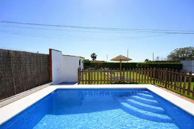 a swimming pool with a fence and an umbrella at Chalet Atardecer in Conil de la Frontera