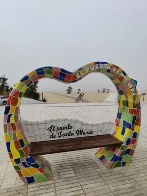 a bench with a heart shaped sculpture in front of a beach at Adelitas Home El Puerto in El Puerto de Santa María