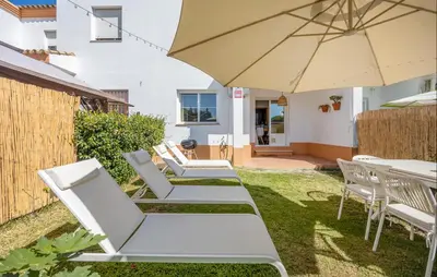 a row of white lounge chairs and an umbrella at Nice Home In Chiclana De La Fronter in Novo Sancti Petri