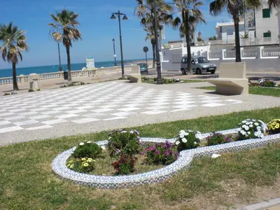a park with flowers and palm trees next to the beach at Holiday Home Touristenwohnung Apartment mit Terrasse by Interhome in Chipiona