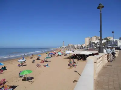 a beach with people sitting on chairs and umbrellas at Apartment Wohnung 'Caracola' mit Terrasse by Interhome in Chipiona