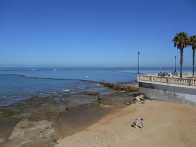 two people walking on the beach near the ocean at Apartment Wohnung 'Caracola' mit Terrasse by Interhome in Chipiona