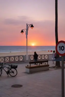 a woman sitting on a bench on the beach at sunset at BARLOVENTO Family Home by Cadiz4Rentals in Cádiz