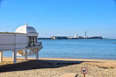 a building on the beach next to the water at Apartamento Plaza Falla Caleta in Cádiz