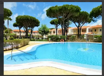 a large swimming pool with trees in the background at La Balconera Apartamento junto a la playa in Novo Sancti Petri