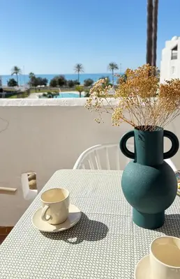 a table with a green vase and a cup on it at Apartamento Marea en primera línea de playa en La Barrosa con vistas al mar in Novo Sancti Petri