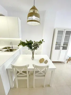 a white kitchen with a table and a vase with flowers at El Arrecife - Apartamento a 2 minutos de la playa en El Puerto de Santa María in El Puerto de Santa María