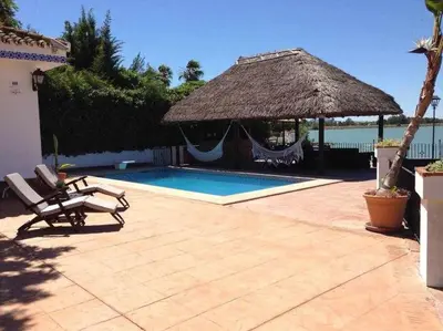 a swimming pool with a straw umbrella and a chair at Espectacular casa con embarcadero. in Arcos de la Frontera
