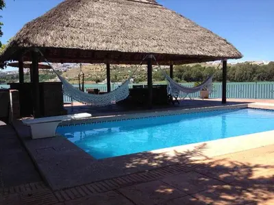 a large hut with hammocks and a swimming pool at Espectacular casa con embarcadero. in Arcos de la Frontera
