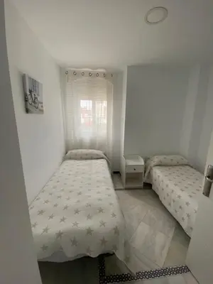 a small bedroom with two beds and a window at Apartamento Medina Puerto Sherry in El Puerto de Santa María