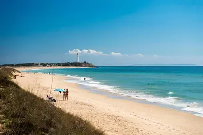 a beach with people and an umbrella and the ocean at Apartamento Oropendola 9 in El Puerto de Santa María