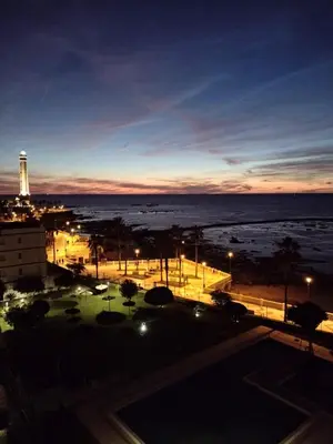 a view of the ocean and a lighthouse at night at Villablanca Apartamento in Chipiona