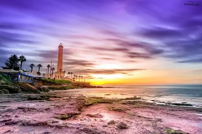 a lighthouse on the beach with a sunset at Villablanca Apartamento in Chipiona