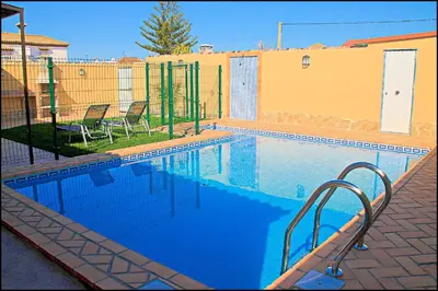 a swimming pool with two chairs and a fence at Bungalow Curro Pareja 131 in Conil de la Frontera
