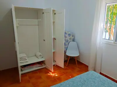 a bedroom with white cabinets and a chair and a window at Chalet Mari Carmen in Chiclana de la Frontera