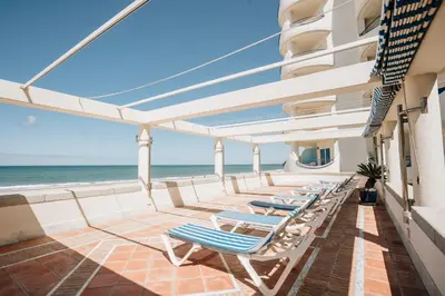 a row of lounge chairs on a balcony overlooking the ocean at Hotel Playa Victoria in Cádiz