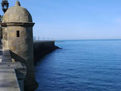 a stone lighthouse next to the water near a pier at La Nube de San Miguel in Cádiz