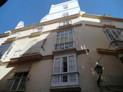 a tall white building with windows and a tower at La Nube de San Miguel in Cádiz