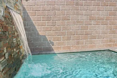 a swimming pool in a brick wall with a water fountain at Bungalow La Roa I in Conil de la Frontera