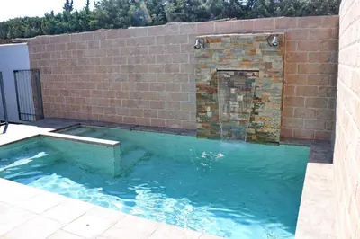a swimming pool with a brick wall and a water fountain at Bungalow La Roa I in Conil de la Frontera