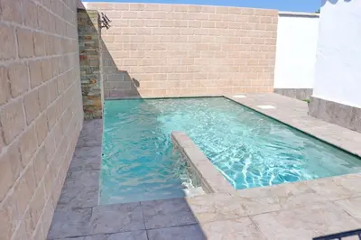 a swimming pool with a brick wall and blue water at Bungalow La Roa I in Conil de la Frontera