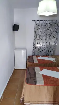 a small room with two beds and a refrigerator at Hostal las Parcelas in Conil de la Frontera