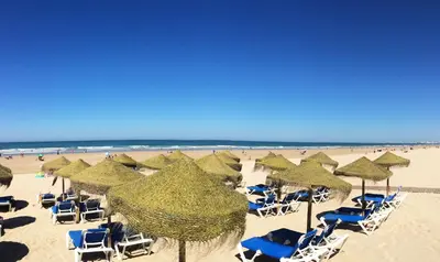 a beach with chairs and straw umbrellas and the ocean at Apartamento Cantabrico in Cádiz